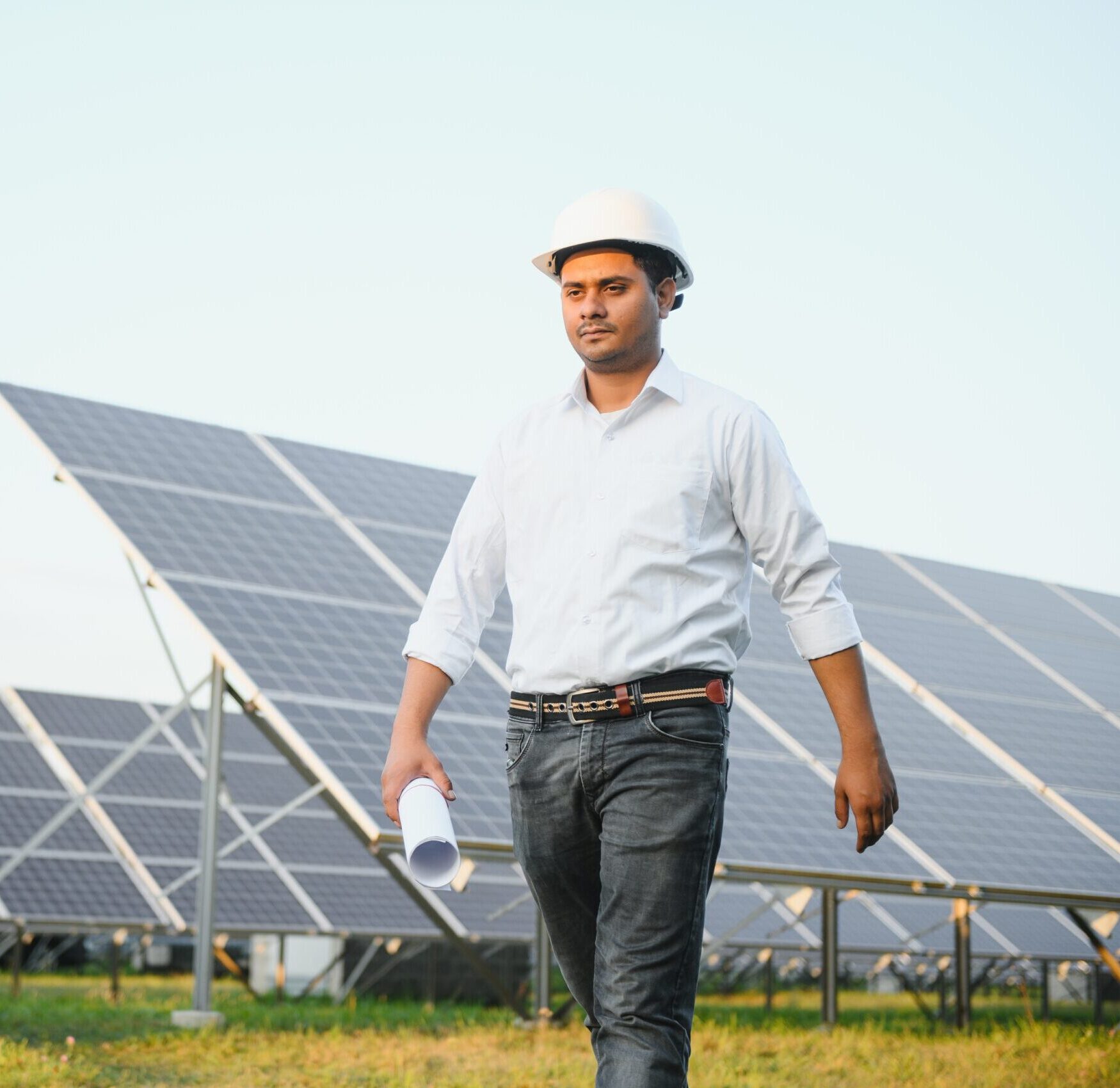 Portrait of Young indian male engineer standing near solar panels, with clear blue sky background, Renewable and clean energy. skill india, copy space.